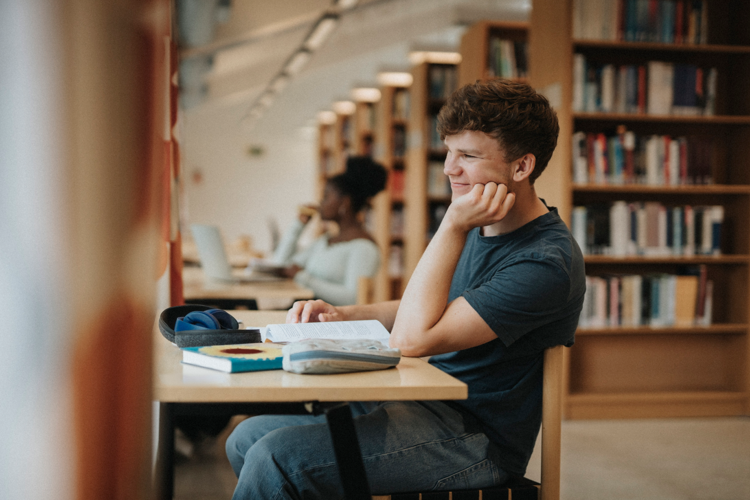 Un estudiante estudiando en un escritorio con libros y un portátil en una biblioteca.
